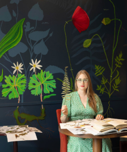 The artist holding a fern with her artwork filling the background